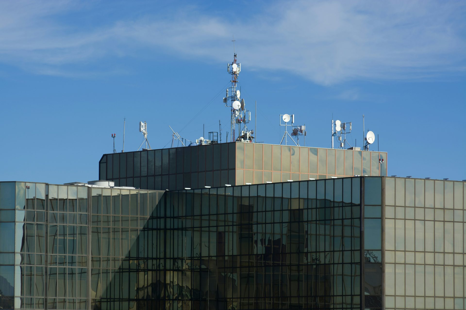 Antennas crown a modern glass building's rooftop.